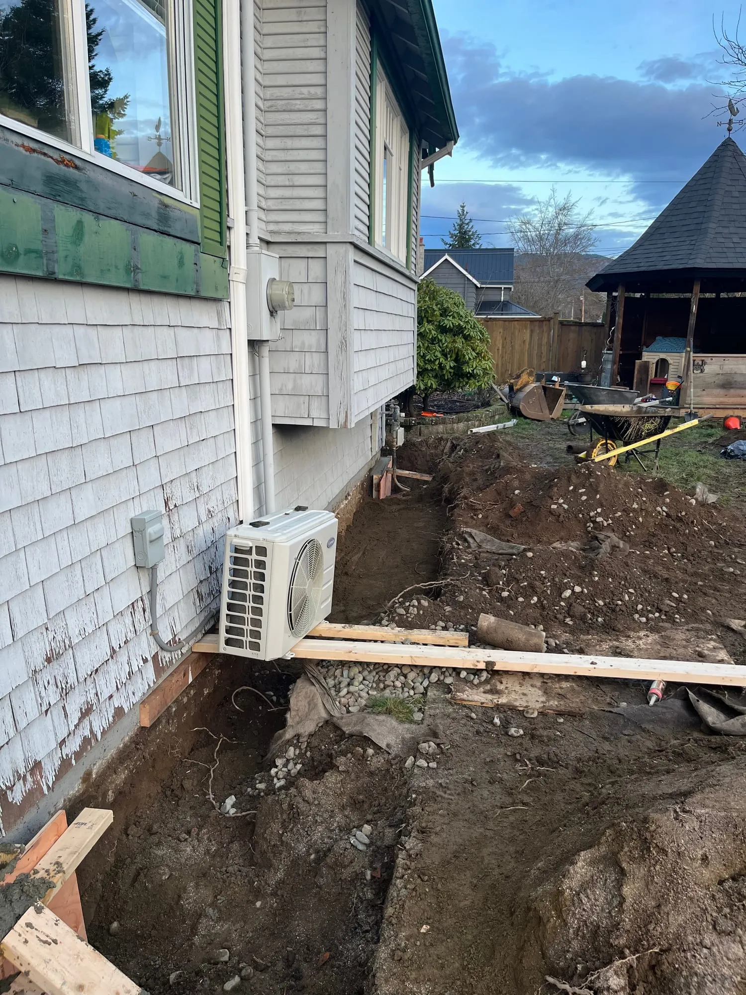 Digging alongside the foundation, working around roots and live utilities.